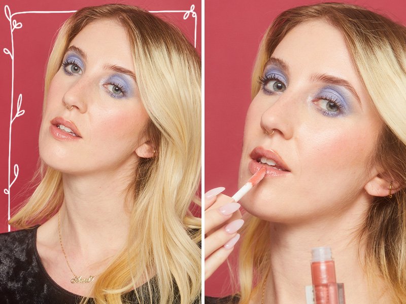 A person with blonde hair and light blue eyeshadow applies pink lip gloss to her lips